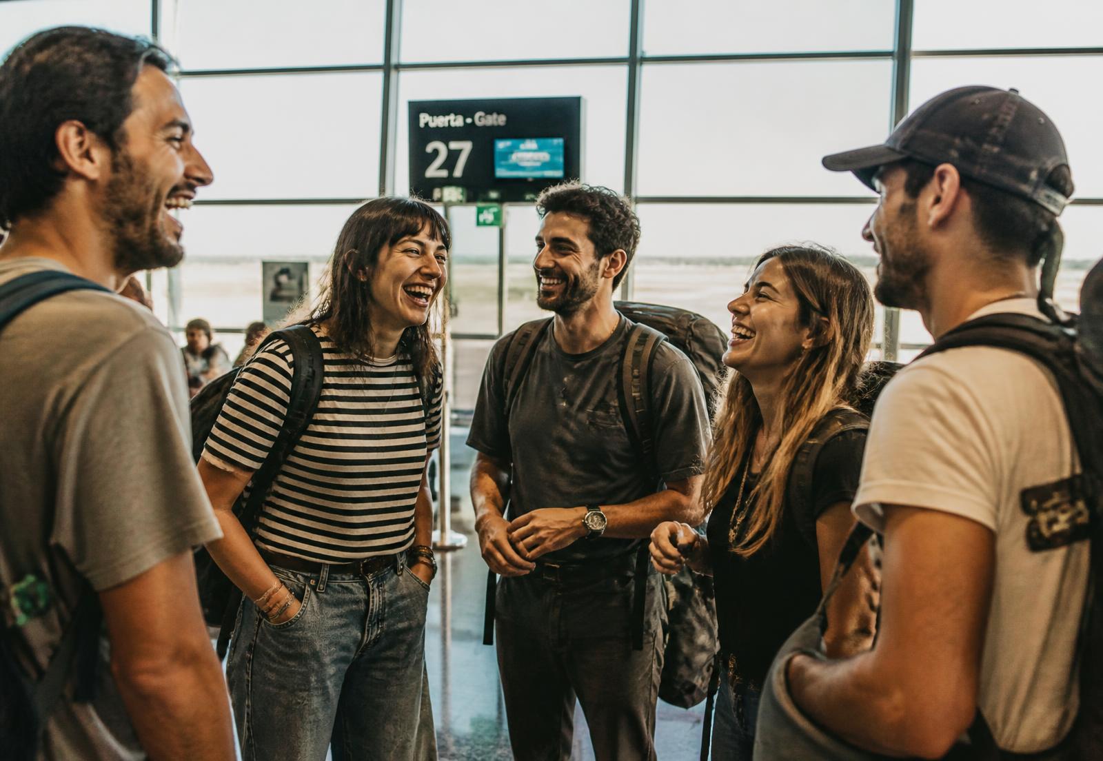 Grupo de viajeros riendo juntos en la puerta de embarque de un aeropuerto
